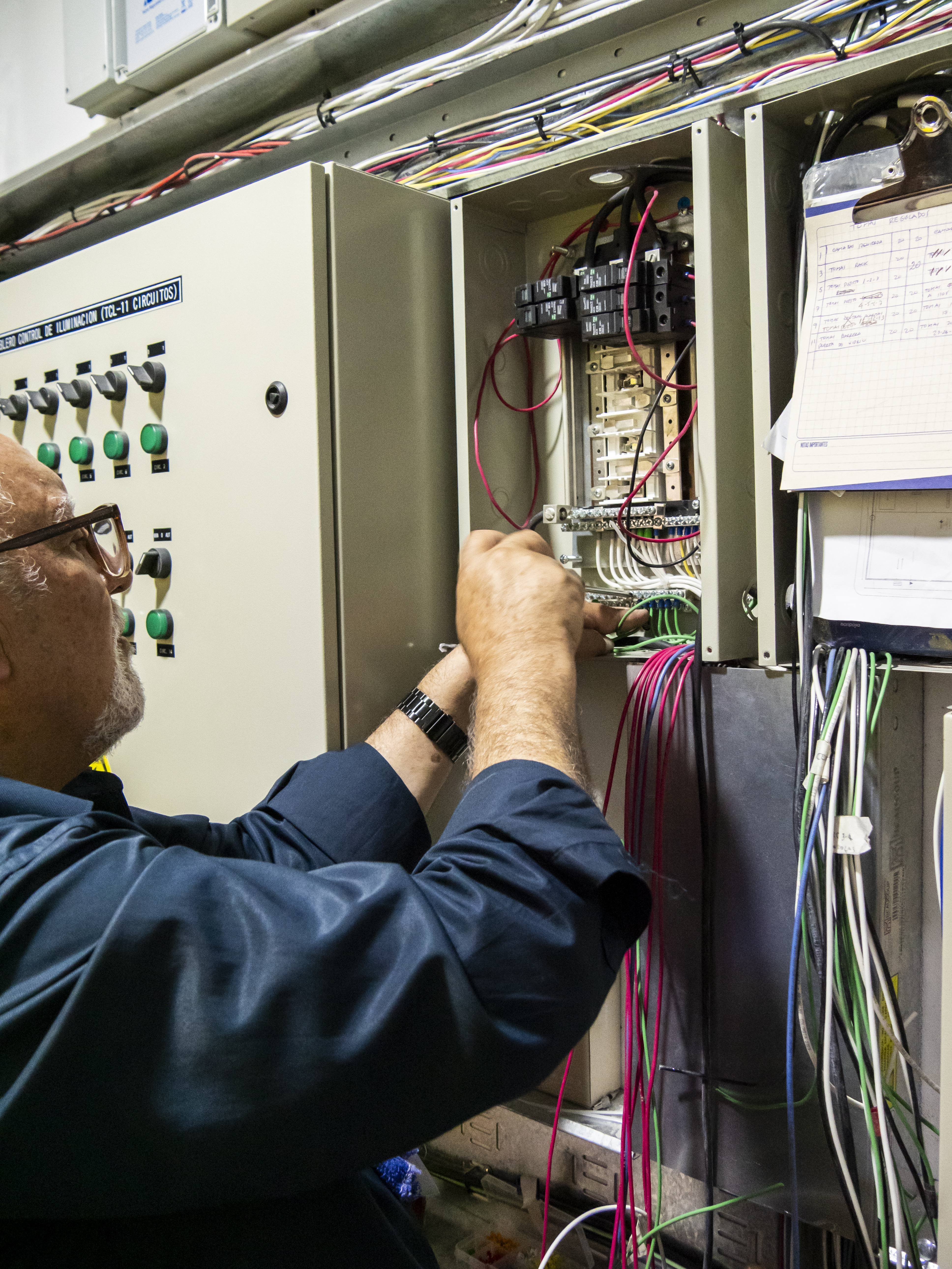 Experienced senior electrician performing electrical maintenance inside a power distribution control panel. Technician installing circuit breakers and organizing wiring in an industrial electrical system, representing skilled labor, engineering work, and energy infrastructure.